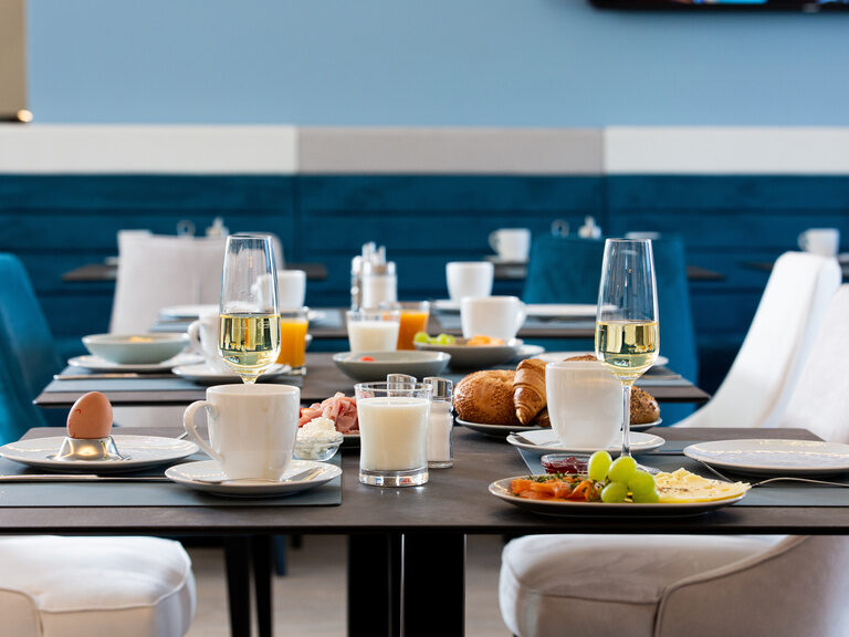 frühstückstisch mit tassen und teller ein glas milch sekt und süßen croissants